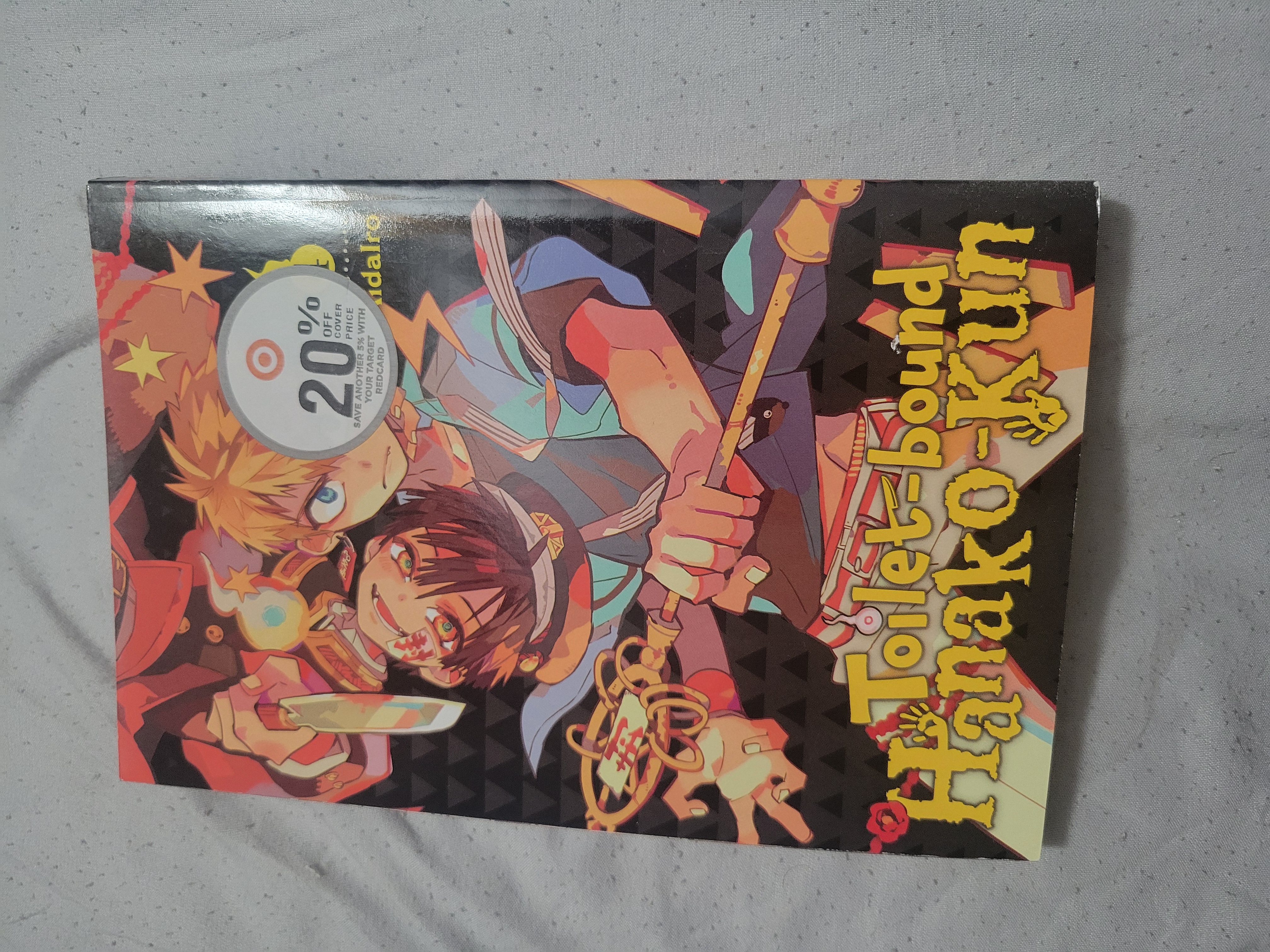 Front cover of Back of Toilet-bound Hanako-kun volume four on a gray bedsheet.